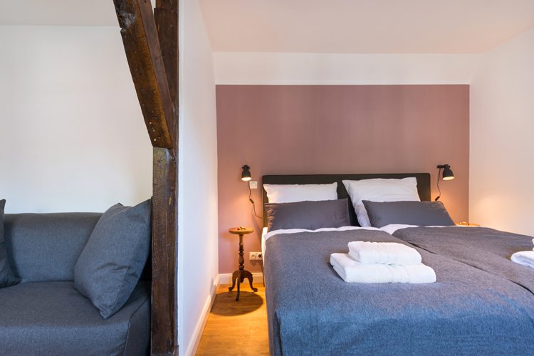 Das Kiepenkerlezemmer: Doppelbett mit blauer Decke, Sessel und Fachwerkbalken